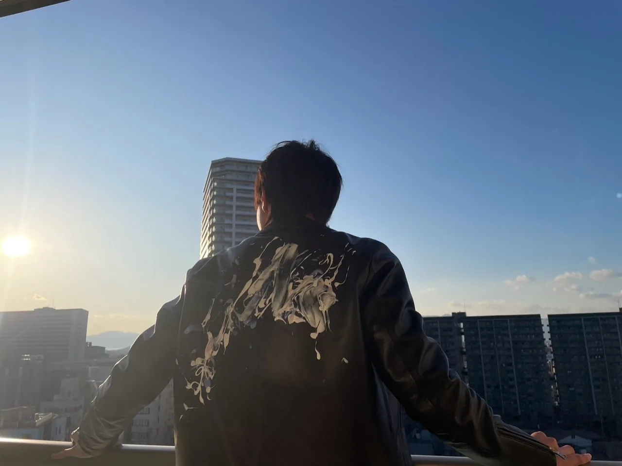 レザージャケットを着て街の夕景を眺める後ろ姿